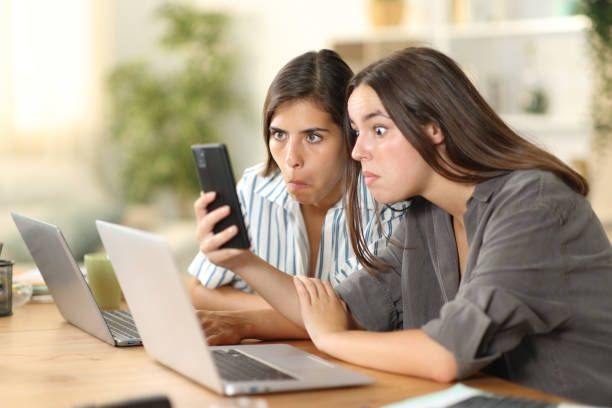 Two female employees read shocking gossip on phone at work