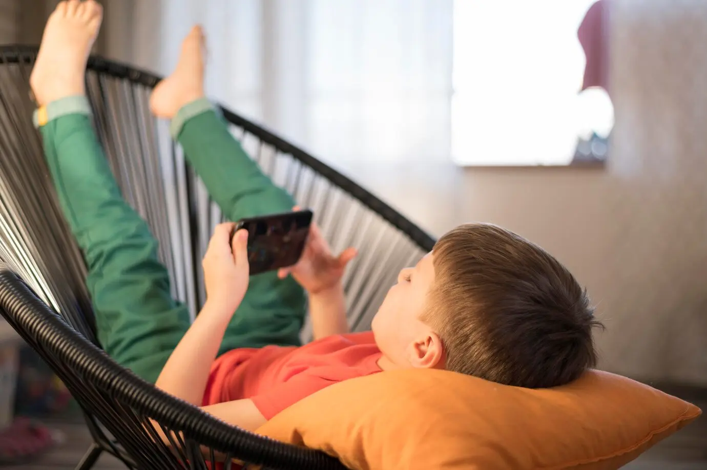 A boy lying on a chair playing with his mobile phone