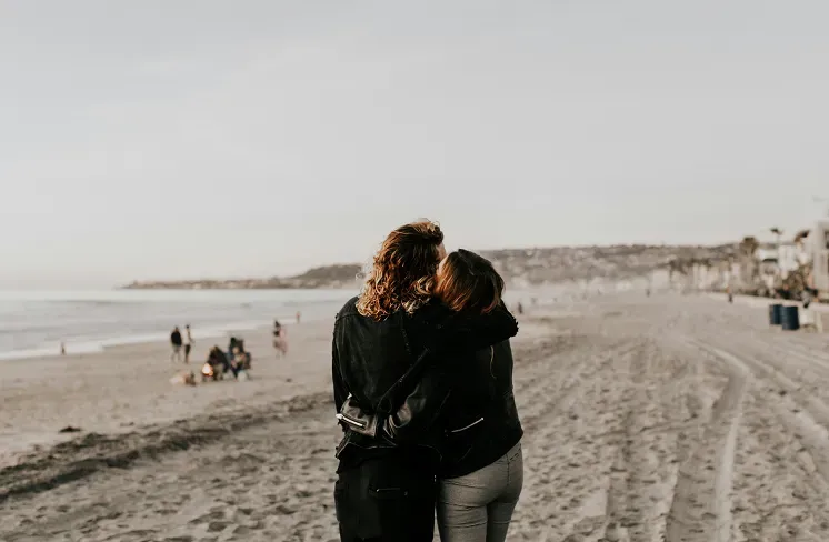 Una pareja camina abrazada por la orilla de una playa al atardecer.
